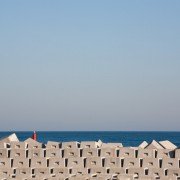 Un muro de hormigón con una bandera roja cerca del océano. Esta imagen cautivadora podría ser capturada por un fotógrafo talentoso especializado en fotografía arquitectónica u hoteles, mostrando realmente su experiencia en la captura de imágenes impresionantes.
