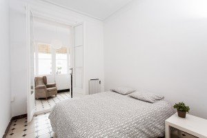 Un dormitorio blanco con una cama y una silla, maravillosamente captado por un profesional de la fotografía de interiores.