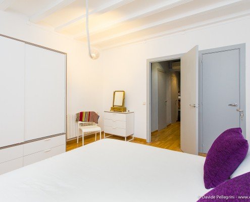 Descripción: Una habitación con una cama blanca y almohadas moradas.