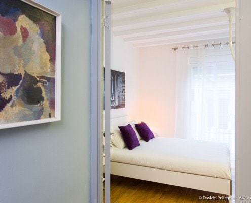 Una cama blanca en una habitación con un cuadro en la pared, capturado en una fascinante fotografía arquitectónica.
