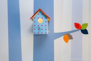 Una pared de rayas azules y blancas con una casa de pájaros en ella.