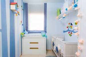 Descripción: Un reportaje fotográfico de un cuarto de bebé en tonos azul y blanco, con una cuna y un tocador.