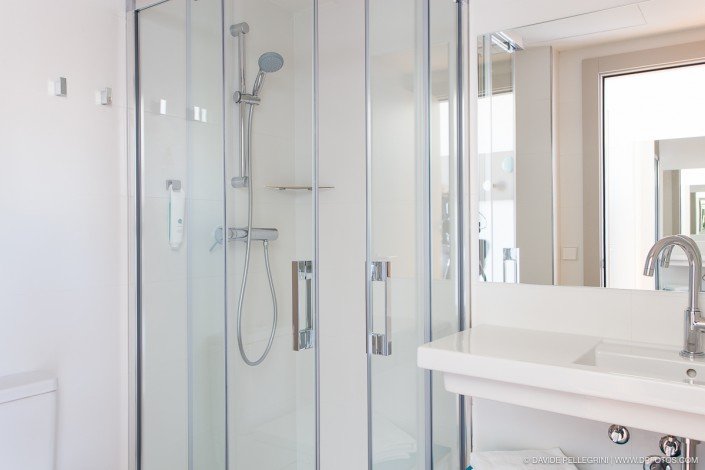 Un baño blanco con cabina de ducha de cristal capturado en una sesión fotográfica de arquitectura.