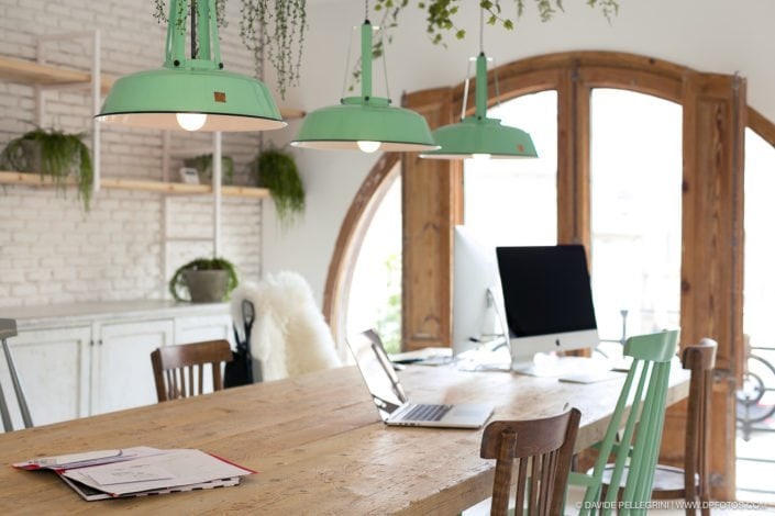 Una oficina en Barcelona reformada con un escritorio de madera y una lámpara verde colgando sobre él.