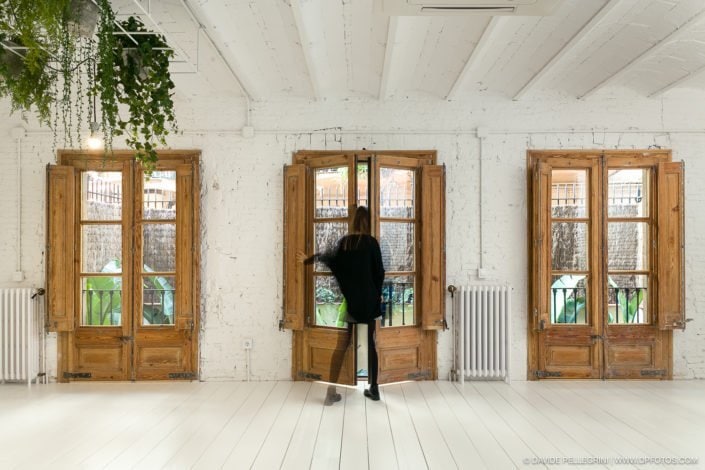 Una mujer parada frente a una habitación con puertas de madera, capturando a través de la fotografía la esencia de la renovación de oficinas en Barcelona.