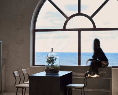 Una mujer sentada en una mesa en una habitación con vista al océano para un reportaje fotográfico.
