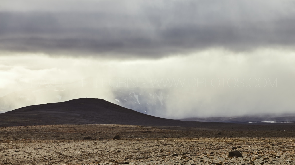 Un hombre está parado bajo un cielo nublado con una montaña al fondo, capturado por un fotógrafo.