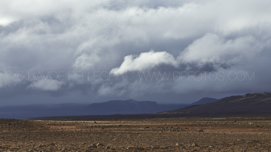 Un cielo nublado sobre un paisaje árido con montañas al fondo capturado por un fotógrafo de arquitectura.