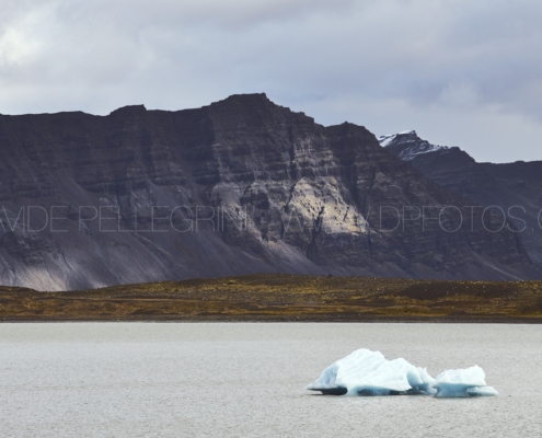 Un iceberg flotando en un lago con montañas de fondo. Fotografía.