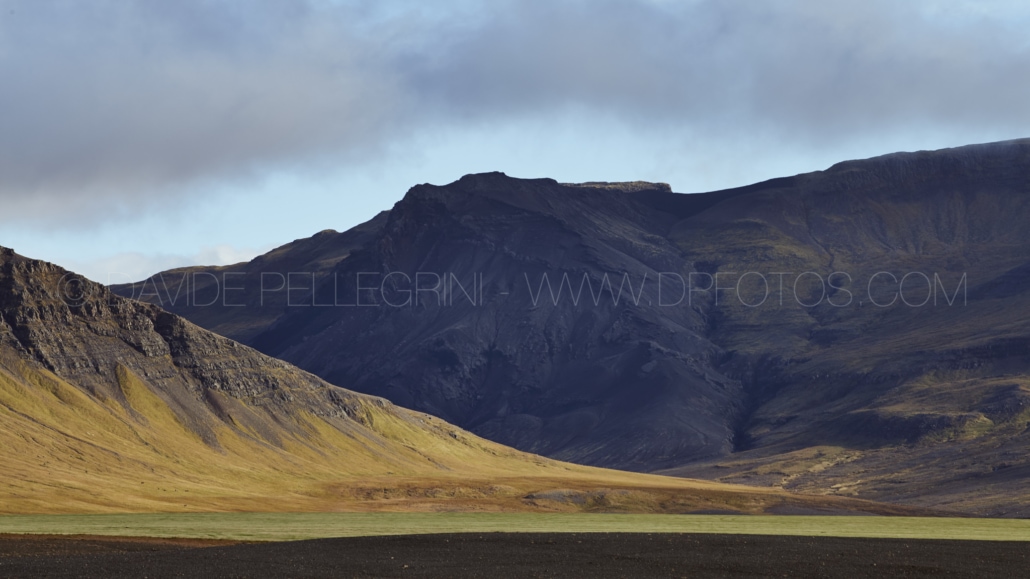 Una pintoresca cadena montañosa con un campo de hierba y un cielo nublado, capturada por un fotógrafo talentoso con ojo para paisajes impresionantes.