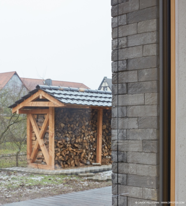 Descripción: Un reportaje arquitectónico de un cobertizo de madera con troncos frente a él.