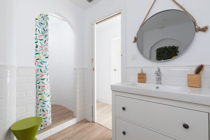 Un baño blanco con un taburete verde y una cortina de ducha, con un bonito diseño interior.