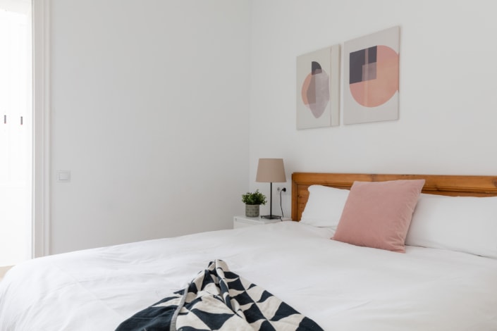 Descripción: Un dormitorio con una cama blanca y almohadas rosas.