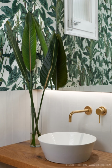 Un baño con papel pintado tropical y lavabo dorado