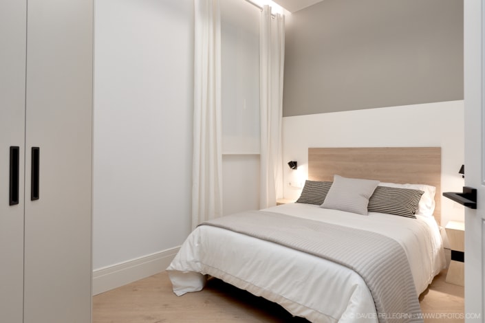 Un dormitorio con una cama blanca y paredes grises que muestra un diseño de interiorismo moderno.