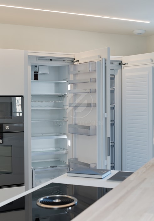 Un refrigerador abierto en una cocina, presentado en un reportaje inmobiliario de alta gama.