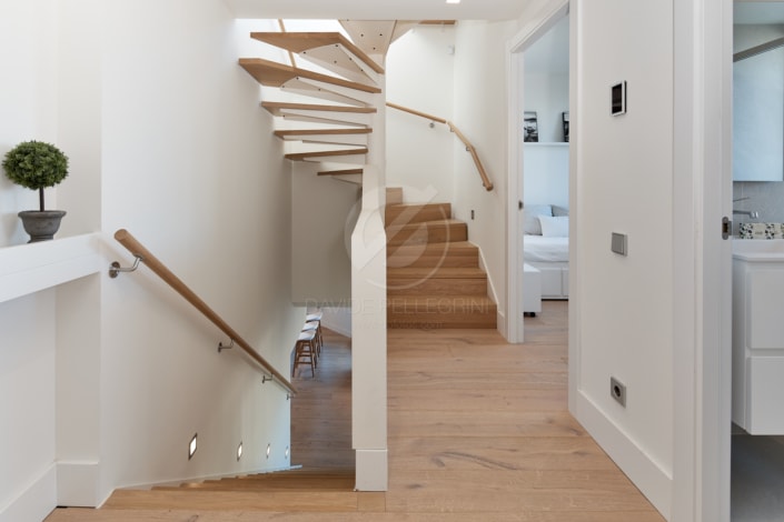 Un reportaje inmobiliario di alto standing de una elegante escalera en espiral en una casa blanca con pisos de madera.