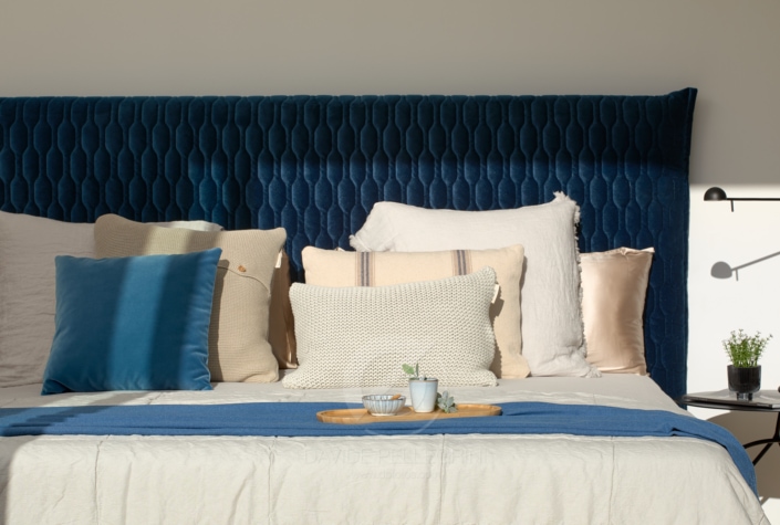 Una cama con cabecero azul y almohadas blancas, captada por un talentoso fotógrafo especializado en diseño de interiores.