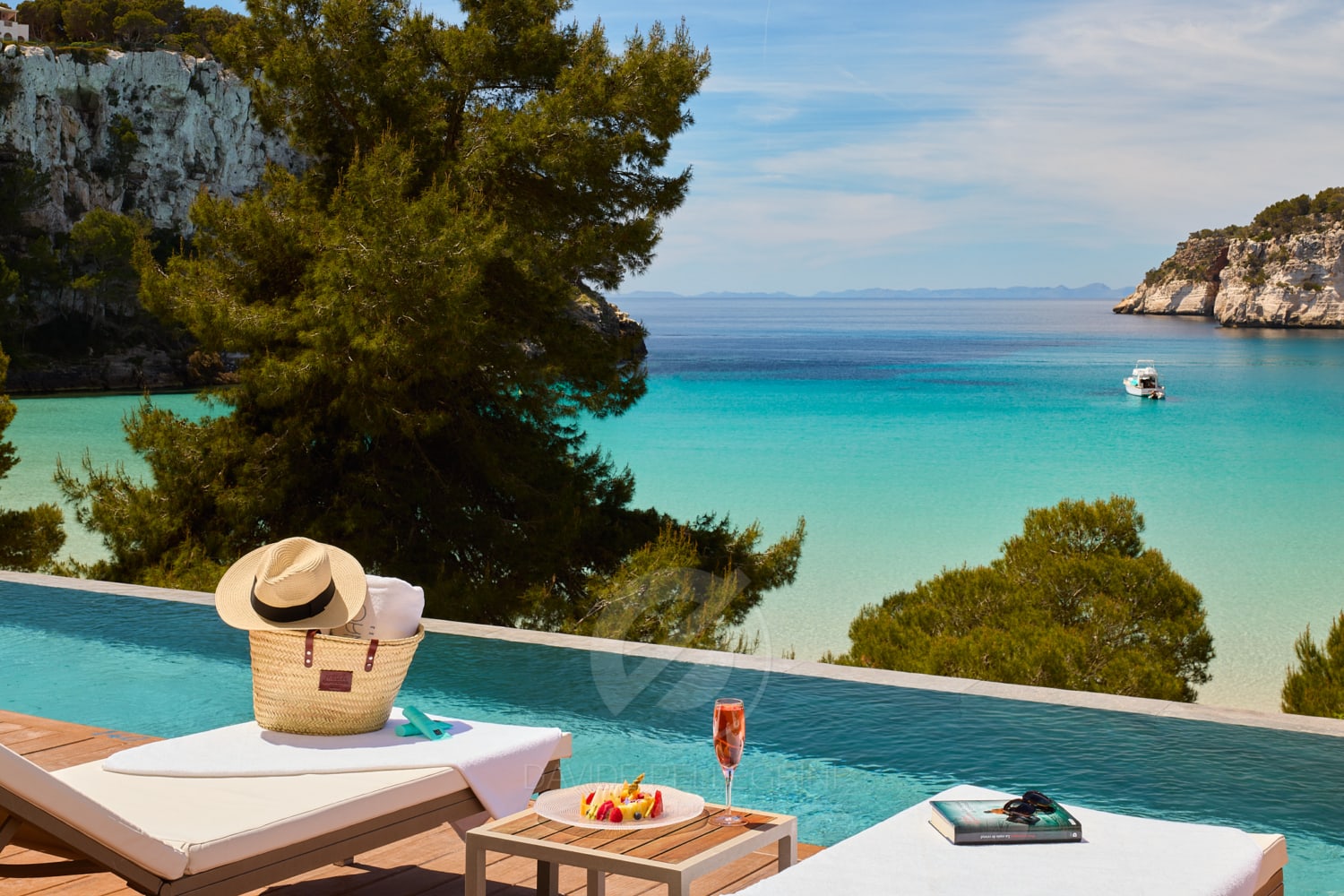 Una mujer sentada en un sillón junto a una piscina, disfrutando de la hermosa vista del océano en Menorca, capturada por un experto fotógrafo de hotel.
