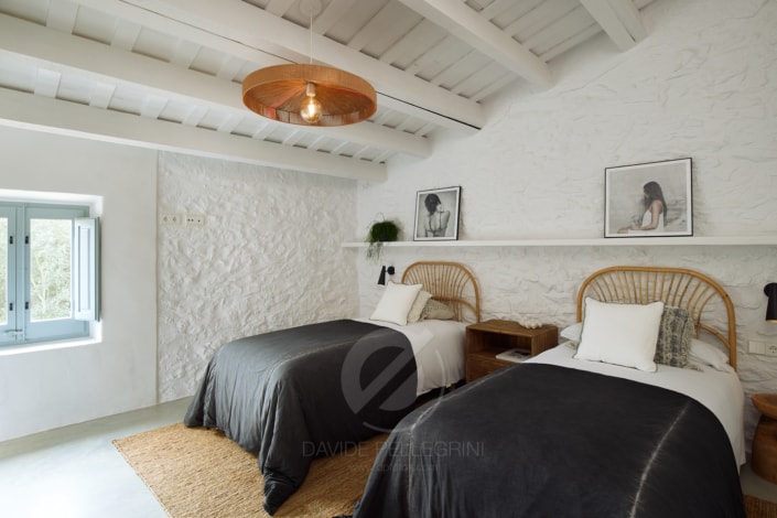 Dos camas en un dormitorio de paredes blancas y vigas de madera, captadas por un talentoso "Fotógrafo de masías".