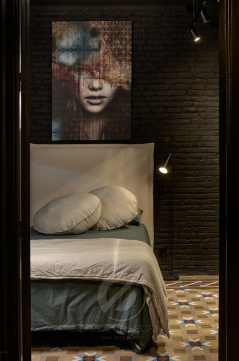 Un dormitorio con una cama y un cuadro en la pared, capturado por un talentoso fotógrafo que muestra maravillosamente los elementos de interiorismo del espacio.