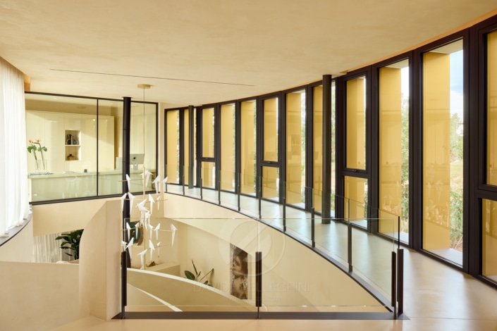 Una escalera curva alta se exhibe en una casa moderna durante una sesión fotográfica para una agencia inmobiliaria.