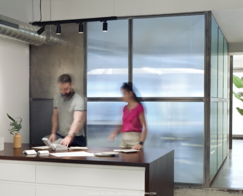 Dos personas trabajando en un espacio de oficina de estudio de diseño con mamparas de vidrio translúcido.