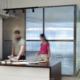 Dos personas trabajando en un espacio de oficina de estudio de diseño con mamparas de vidrio translúcido.