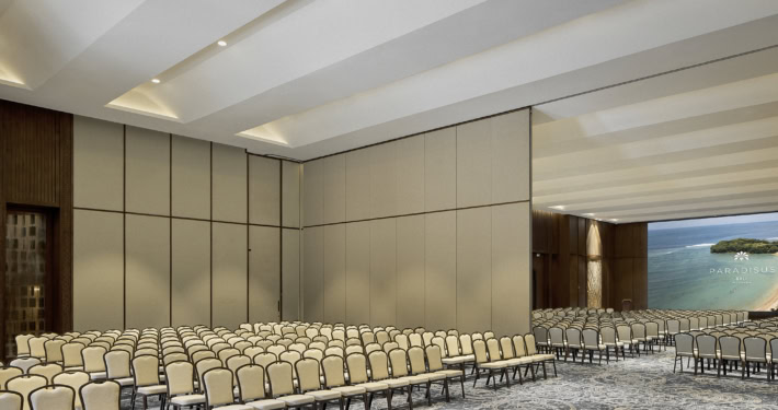 Amplio salón con filas de sillas beige y paredes neutras, ideal para eventos y presentaciones.